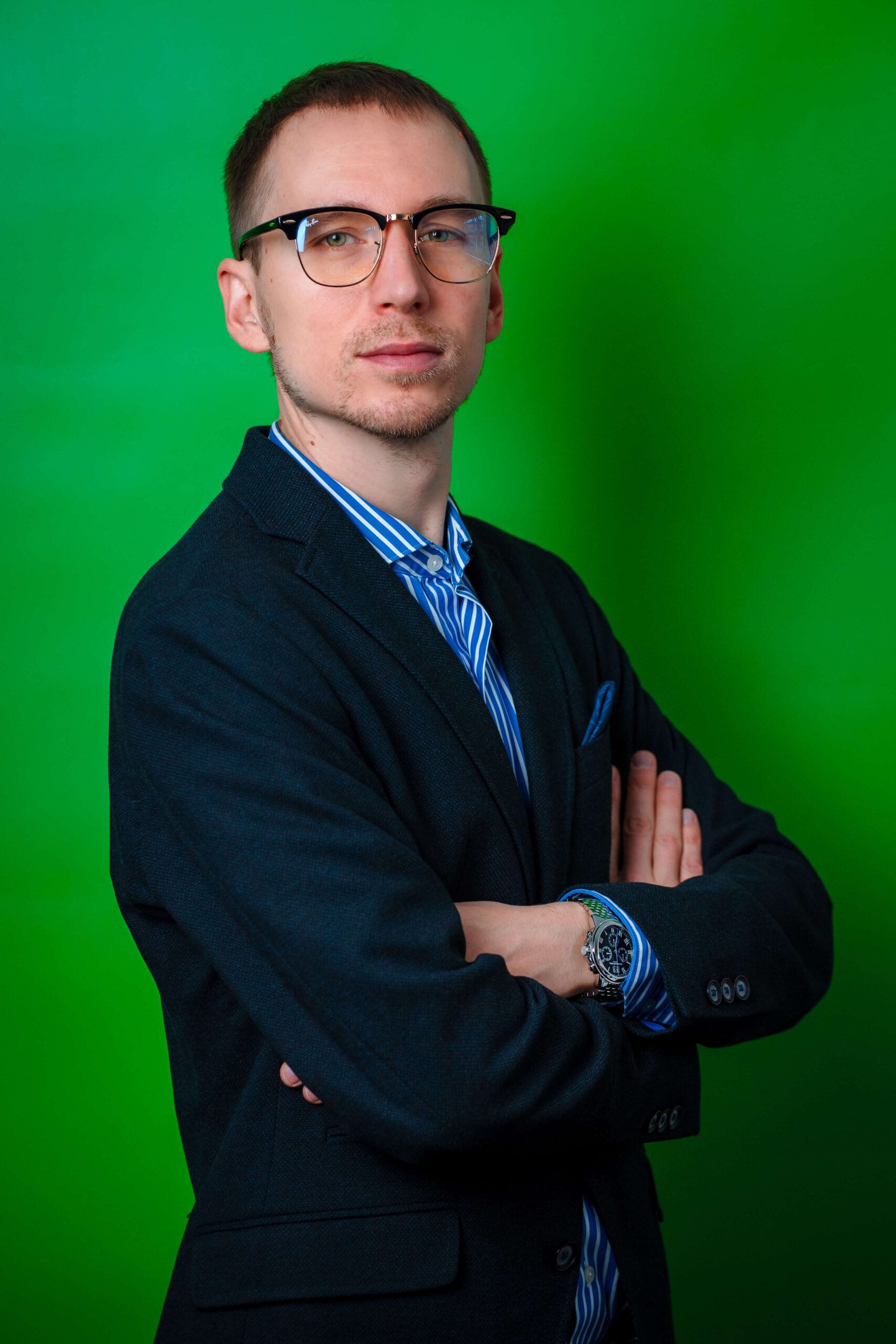 Portrait of the manager of Express Heroes, Mr. S. Mozgovoi, wearing a dark jacket with a white and blue shirt, standing with his arms folded in front of a green background